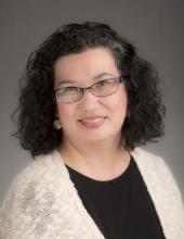 Head and shoulders shot of Sunni Nishimura. She smiles at the camera. She has shoulder lenght wavy black hair and glasses.