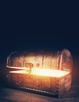 A wooden treasure box that is slightly ajar - light glows from within the box. Background is black.