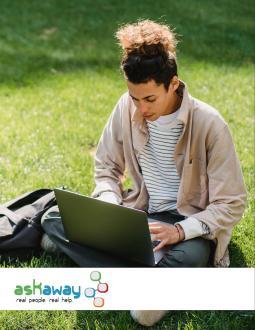 Post-secondary student sits cross-legged on green grass, with laptop on lap. He is working.